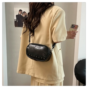 Fashionable black leather crossbody bag with silver studs worn by a model in a yellow suit