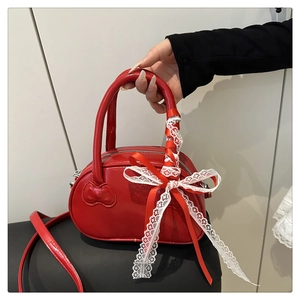 Detail of red patent leather shell bag with lace bow and white ribbon handle decoration