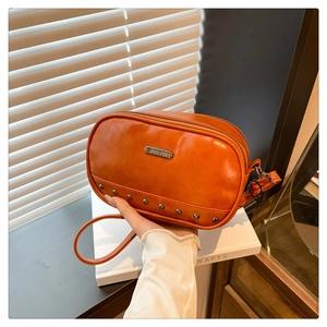 Detailed close-up of orange faux leather crossbody bag with metal rivets and logo plate