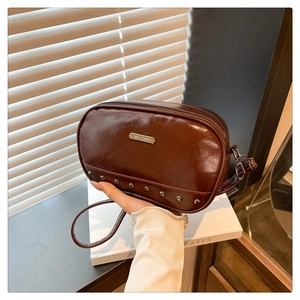Close-up of glossy brown crossbody bag with silver rivet details and metal logo plate