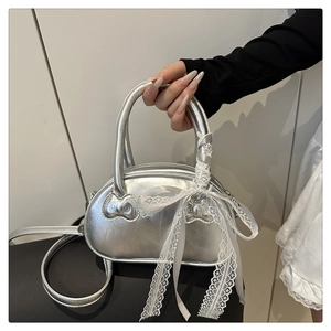 Detail of silver shell bag featuring cat-shaped hardware and a white lace bow accent