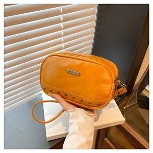 Detail of yellow mini crossbody bag with silver rivets and metal brand plaque