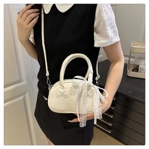 Close-up of beige shell handbag featuring embossed bows and delicate lace ribbon detail