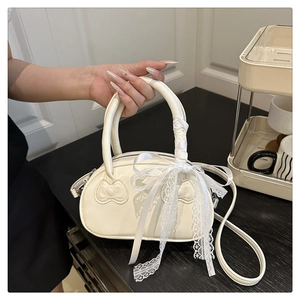 Detail of cream white shell bag with embossed bows and delicate lace ribbon accent