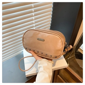 Detail shot of a light brown rivet crossbody bag with a metal logo plate and smooth texture