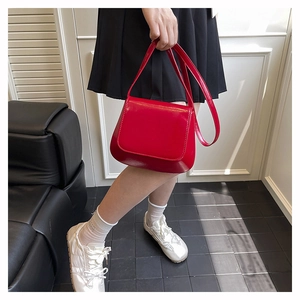 Detail of red glossy saddle bag with curved silhouette and minimalist flap closure