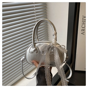 Detail of silver metallic shell bag with cat head embossing and white lace bow