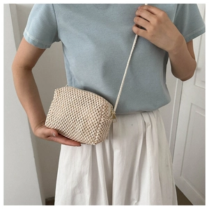 Detail showing the beige hand-woven mini crossbody bag with zipper and slim shoulder strap