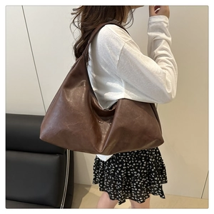 Detail shot of large brown leather hobo bag with wide shoulder strap worn by a model