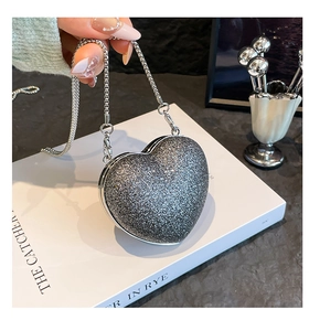 Close-up of heart-shaped glitter evening bag with silver chain on textured background