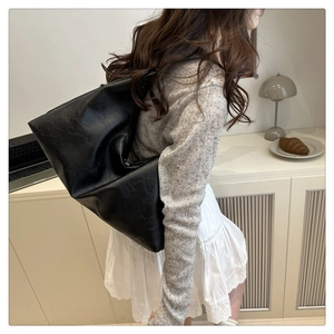 Minimalist black faux leather tote bag worn by a model in a cozy lifestyle setting