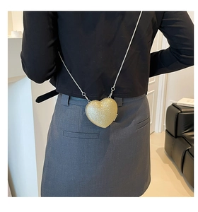 Detail of a heart-shaped crossbody bag with gold sequins and a delicate silver chain strap