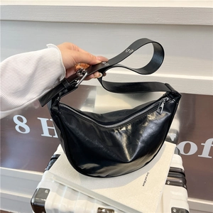 Modern black hobo saddle bag with wide shoulder strap and silver zipper on white luggage