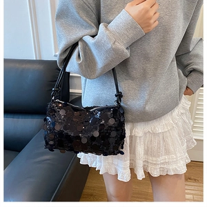 Detail showing the textured black sequins and knotted leather strap of the baguette bag