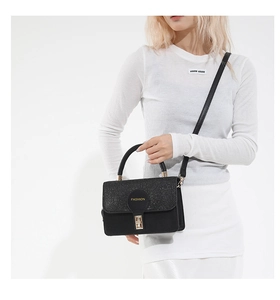 Detail of black vintage square bag with glitter flap and golden metal buckle on model