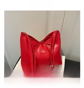 Detailansicht rote Leder-Eimertasche mit Schleife und Logo-Patch auf weißen Büchern