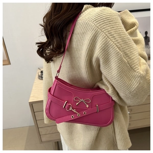 Detail of rose pink shoulder bag with metal bow accent and gold-tone hardware