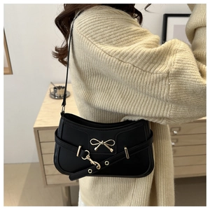 Detail der schwarzen Achseltasche mit goldener Schleife und Ösenriemen auf beigem Pulli