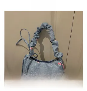 Detailed macro view of denim crescent bag with embroidered pink roses and bow accents
