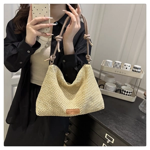 Detail of woven straw tote bag featuring a leather fashion label and knotted handle straps