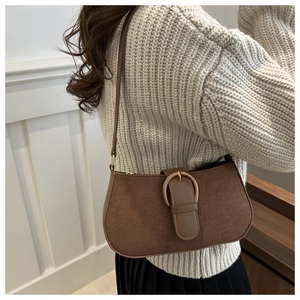 Detailansicht einer braunen Wildleder-Achseltasche mit goldener Schnalle an der Schulter
