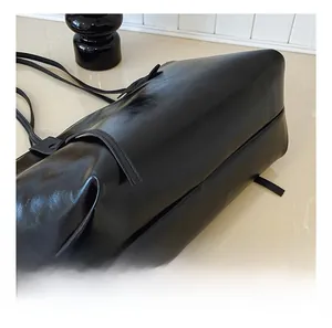 Detail view of smooth black leather texture and side strap of the stylish tote bag