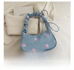 Detailed close-up of floral embroidery and pink bow on blue denim shoulder bag