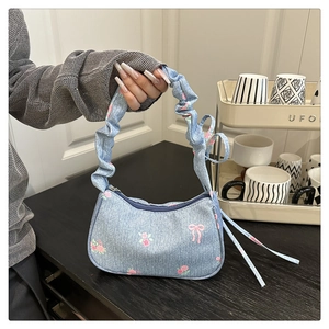 Detail of light blue denim underarm bag with pink floral prints and ruffled handle
