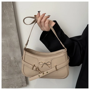 Détail d'un sac sous le bras beige vintage avec boucle nœud doré et sangle à œillets