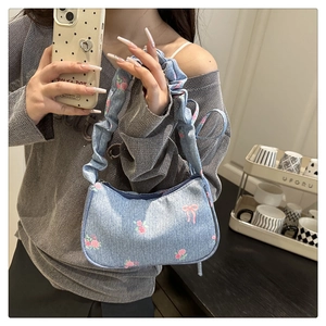 Close-up of light blue denim underarm bag with pink rose prints and pleated shoulder strap