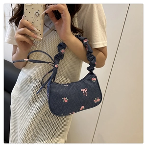 Detail showing blue denim underarm bag with pink floral embroidery and pleated strap