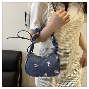 Detail of floral denim underarm bag with ruffled strap and pink bow prints