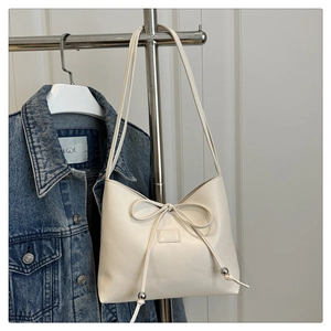 Detailed close-up of cream PU leather handbag with ribbon bow and silver metal beads
