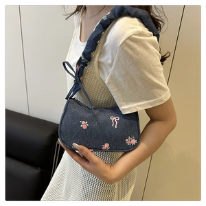 Close-up of denim underarm bag with pink rose embroidery and ruffled strap details