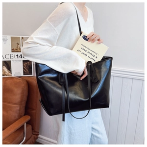 Detailed view of large black glossy leather tote bag worn by a model in a home setting
