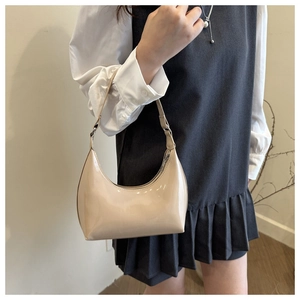 Close-up of minimalist glossy cream hobo bag worn by model with sleek patent finish