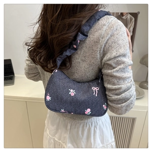 Detail of dark blue denim underarm bag with pink rose prints and ruffled shoulder strap