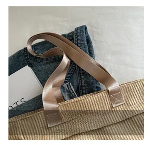 Top view of beige woven tote bag with brown handles on white fabric and denim