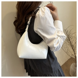 Side view of a white patent leather hobo shoulder bag worn on a woman's shoulder