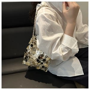Detail of gold sequin bucket bag with metal chain strap worn by a model in a party setting