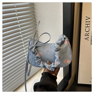 Detail of light blue denim underarm bag featuring pink rose floral print and ruffled handle