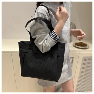 Detail shot of black tote bag featuring textured fabric and functional side pocket