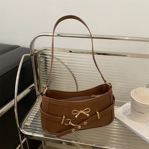 Braune Halbmod-Schultertasche aus Kunstleder mit goldener Schleife auf einem Regal