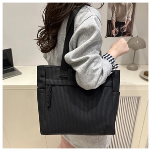 Detailed side view of black woven tote bag with textured stripes and wide shoulder strap