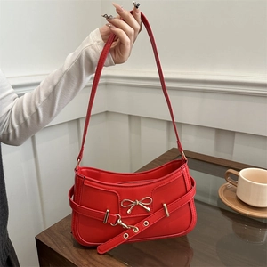 Rote Leder-Schultertasche mit goldener Schleife in einem gemütlichen Café-Ambiente