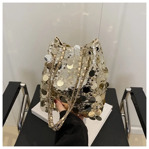 Detail shot of golden sequin bucket bag with chain strap held in hand for party style