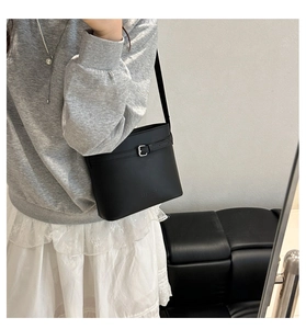 Detail of minimalist black matte leather bucket bag with metallic buckle and shoulder strap