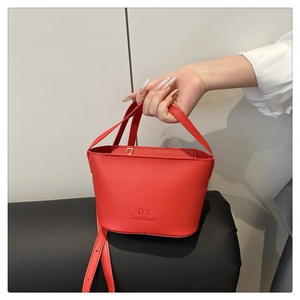 Gros plan sur un sac seau en cuir rouge avec poignée courte et détails métalliques polis