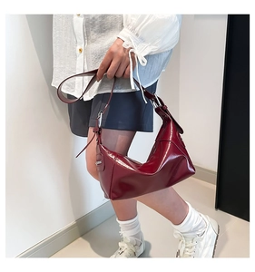 Model wearing a burgundy patent leather crescent underarm bag with silver hardware