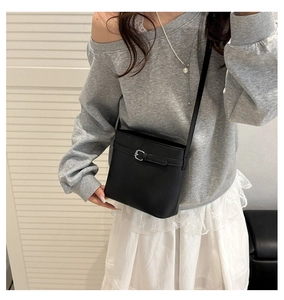 Detailed view of black litchi texture bucket bag with silver buckle worn by a model